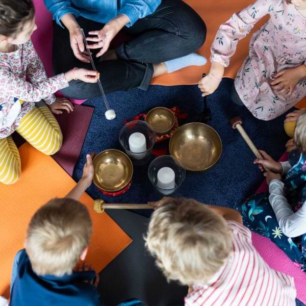 Pädagogin mit Kinder sitzen im Kreis um Klangschalen und arbeiten damit