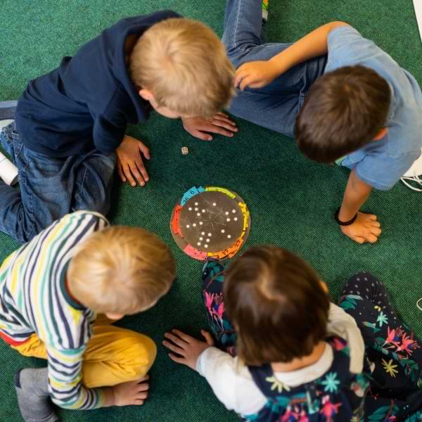 Kinder arbeiten sitzend auf einem Teppich mit Montessori Material
