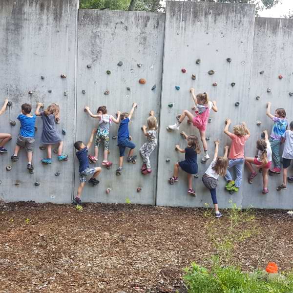 Kinder klettern außen an der einer Wand hoch.